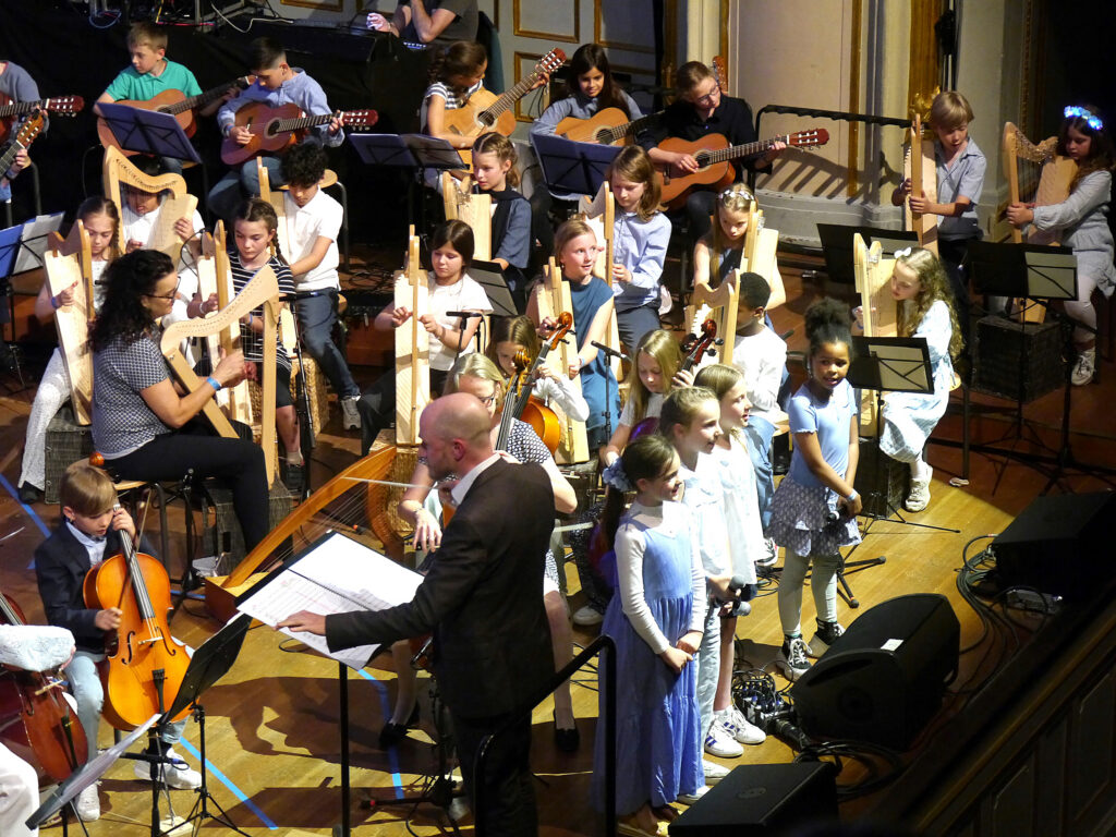 ein Orchester aus Schülerinnen und Schülern mit Gitarren, Celli, Harfen und Gesang auf der Bühne der Hamburger Laeisz-Halle