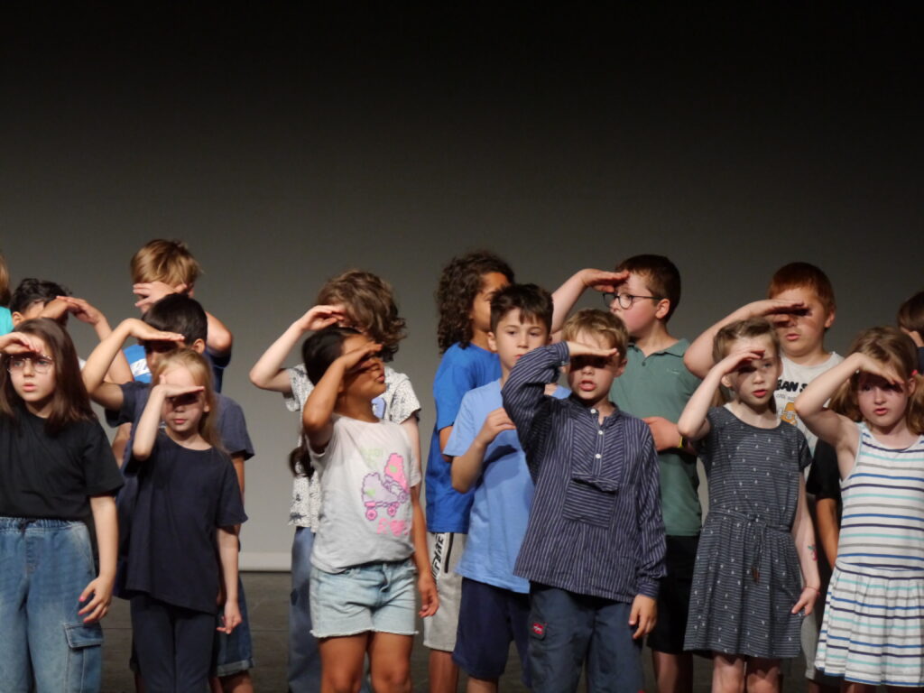 Eine Gruppe von Schüler*innen in einer Theaterszene. Sie schauen in die Ferne und schützen mit einer Hand ihre Augen vor der Sonne.