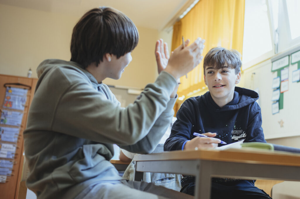 Zwei Schüler sitzen an einem Tisch und besprechen ihre Aufgabe.
