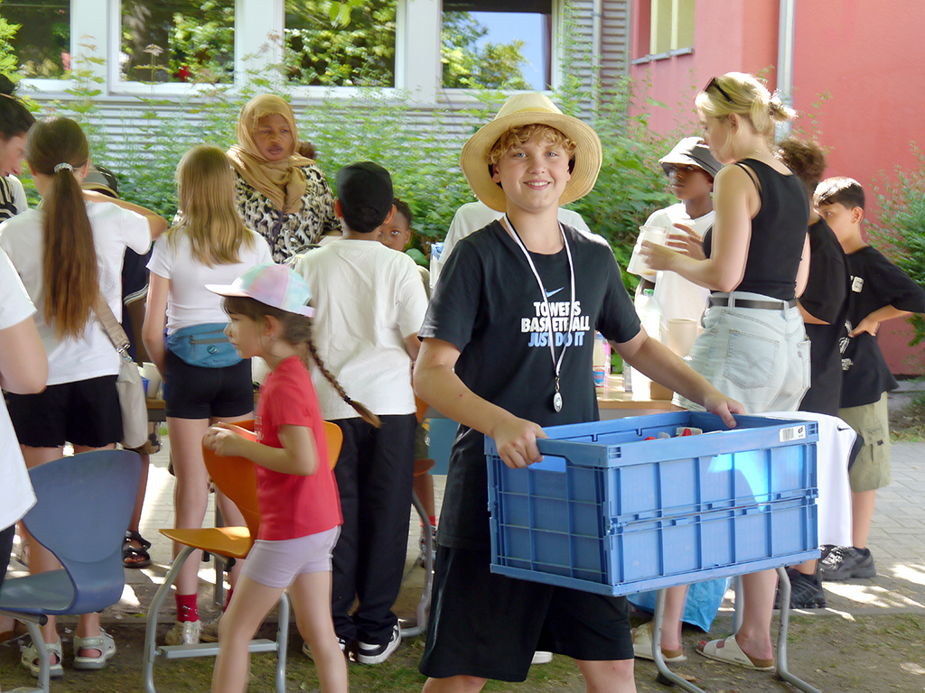Impressionen vom Fest der Vielfalt. Ein Junge trägt eine große Kiste, im Hintergrund Menschen an einem Getränkestand.