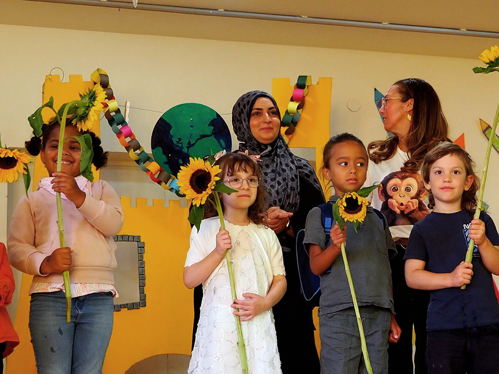 Lehrerinnen der neuen Vorschulklassen mit ihren Kindern auf der Bühne; Die Kinder halten Sonnenblumen in der Hand